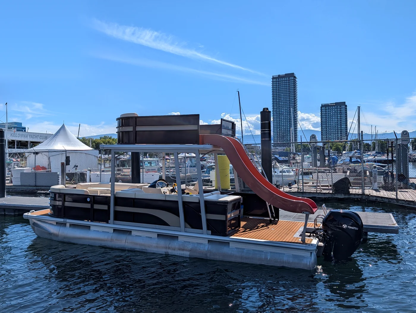 Canalake Boats double decker pontoon with water slide moored in downtown Kelowna, city towers behind